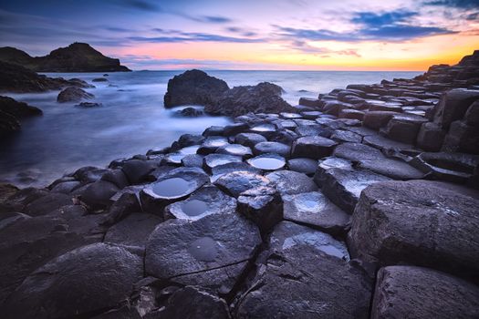 sunset over basalt rocks formation Giant's Causeway, Port Ganny Bay and Great Stookan, County Antrim, Northern Ireland, UK