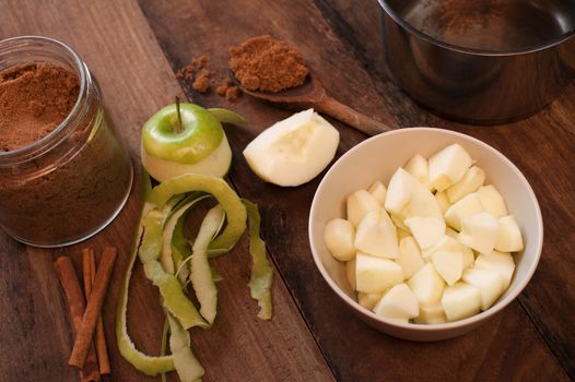 Peeled and diced fresh apple with cinnamon sticks and aromatic ground spice on a wooden spoon ready for use as baking or cooking ingredients