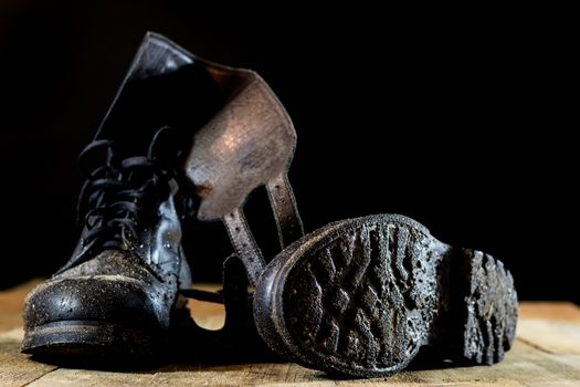 Muddy old military boots. Black color, dirty soles. Wooden table. Black background