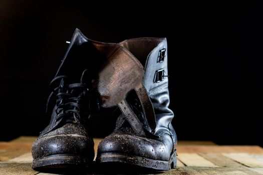 Muddy old military boots. Black color, dirty soles. Wooden table. Black background