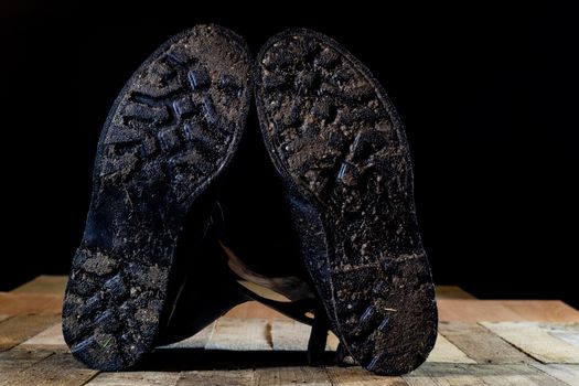 Muddy old military boots. Black color, dirty soles. Wooden table. Black background