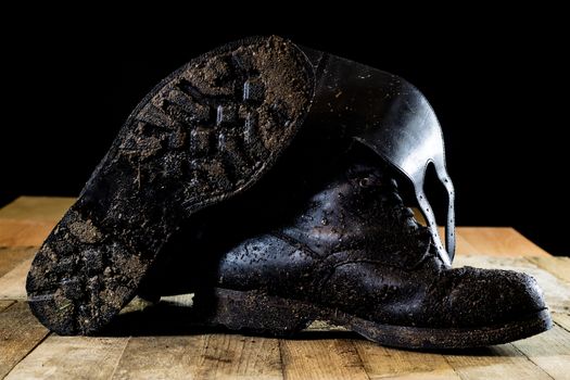 Muddy old military boots. Black color, dirty soles. Wooden table. Black background