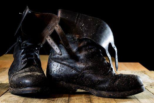 Muddy old military boots. Black color, dirty soles. Wooden table. Black background