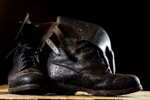 Muddy old military boots. Black color, dirty soles. Wooden table. Black background