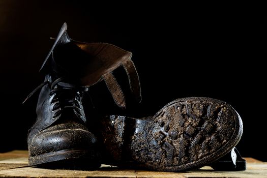 Muddy old military boots. Black color, dirty soles. Wooden table. Black background