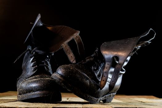 Muddy old military boots. Black color, dirty soles. Wooden table. Black background