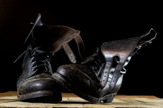 Muddy old military boots. Black color, dirty soles. Wooden table. Black background