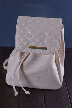 Small white leather female backpack on a black wooden background