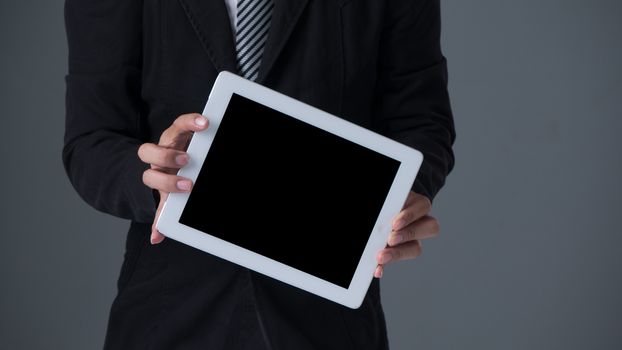 Businessman holding tablet in black suit on gray background