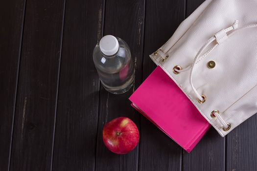 White leather backpack, pink book, bottle of water on a black background