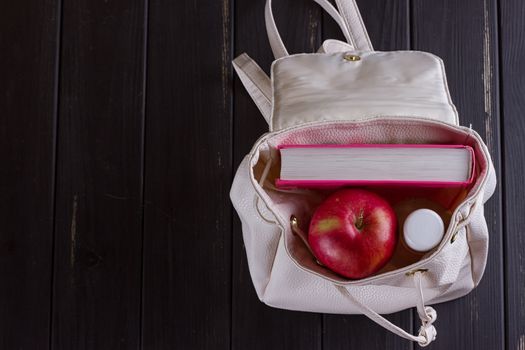 White leather backpack, pink book, bottle of water on a black background