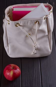 White leather backpack, apple, tube of cream on a black background