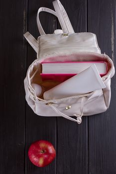 White leather backpack, apple, tube of cream on a black background