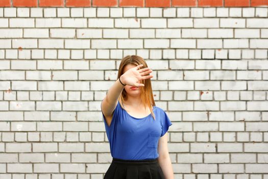 Learning concept. The girl is at the white brick wall. Photo for your design. Holds his hand with the palm of his hand. Prohibition