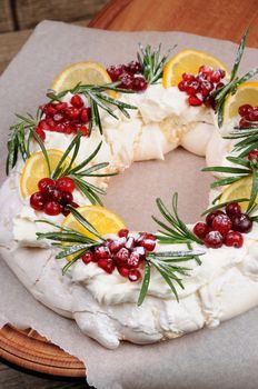 Pavlova cake in the form of a Christmas wreath of meringue with cream, pomegranate, cranberry, rosemary sprigs