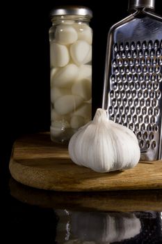 Marinated and fresh garlic with a grater on a dark background