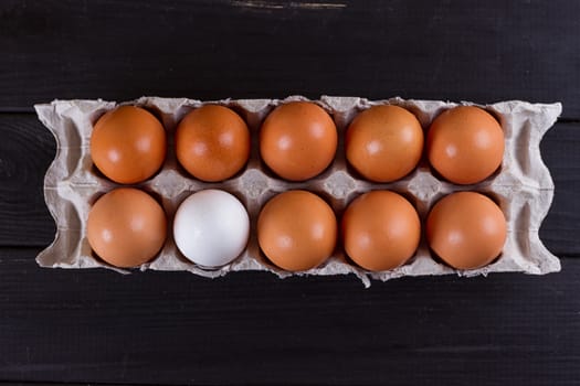Container of ten eggs. Nine eggs brown one egg white. on black wooden background. Eggs container