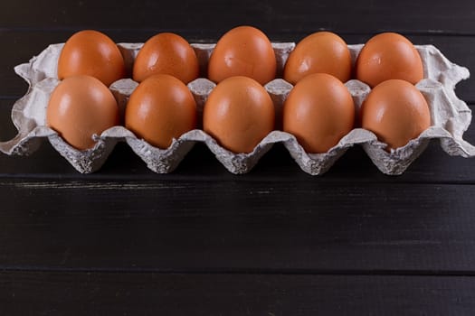 Cardboard egg box on black wooden background. Eggs container