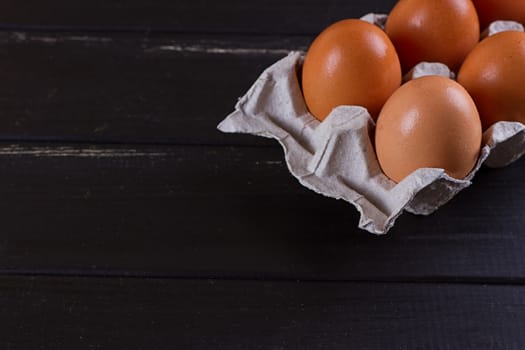 Cardboard egg box on black wooden background. Eggs container