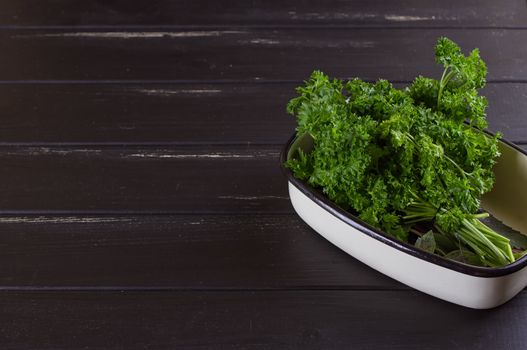 A bunch of fresh parsley in a ceramic tray on a black background. Fresh greens for salad