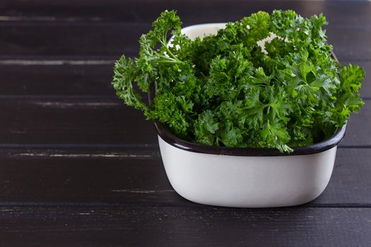 A bunch of fresh parsley in a ceramic tray on a black background. Fresh greens for salad