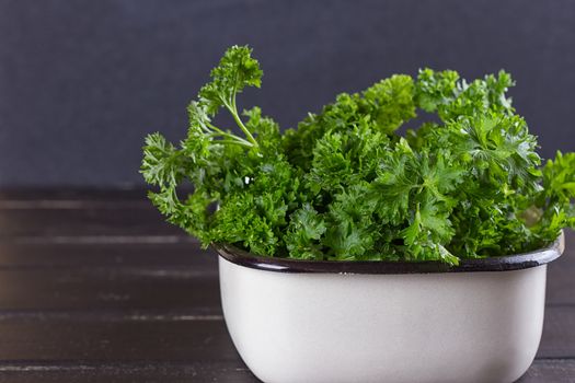 A bunch of fresh parsley in a ceramic tray on a black background. Fresh greens for salad