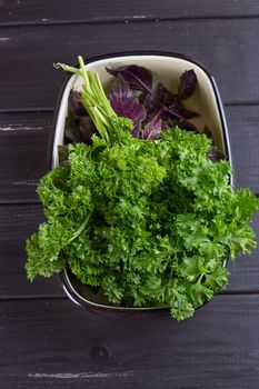 A bunch of fresh parsley in a ceramic tray on a black background. Fresh greens for salad