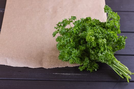 Bunch of parsley and wrapping paper on black wooden background. Copy-space composition