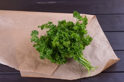 Bunch of parsley and wrapping paper on black wooden background. Copy-space composition