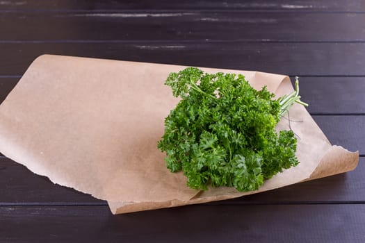 Bunch of parsley and wrapping paper on black wooden background. Copy-space composition