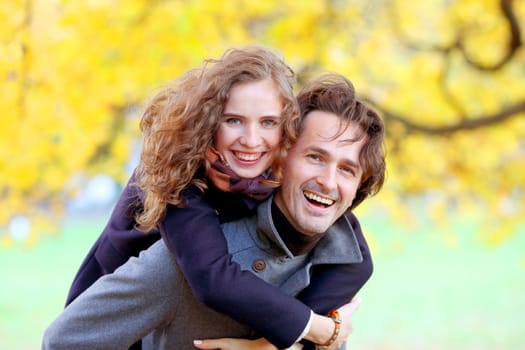 Love, relationships, season and people concept - happy young couple having fun in autumn park piggyback ride