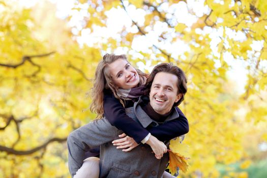 Love, relationships, season and people concept - happy young couple having fun in autumn park piggyback ride