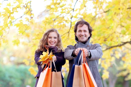 Cheerful couple with shopping bags in autumn park