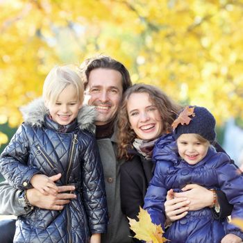 Portrait of happy smiling family with two children relaxing in autumn park