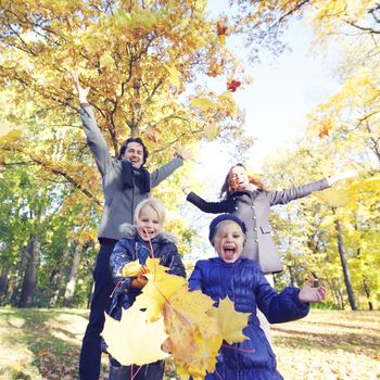Happy family playing with autumn maple leaves in park