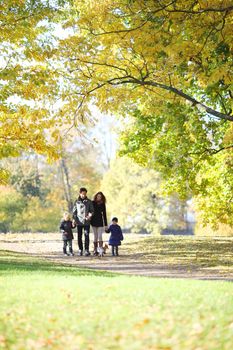 Happy family with two children walking in autumn park holding hands