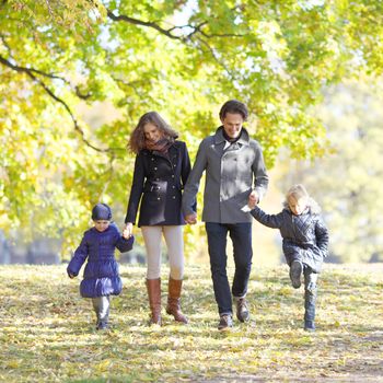 Happy family with two children walking in autumn park holding hands