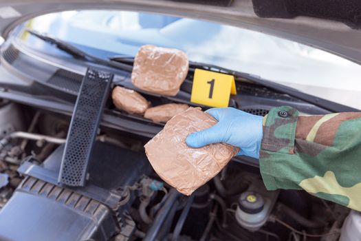 Police officer holding drug package discovered in engine compartment of a car