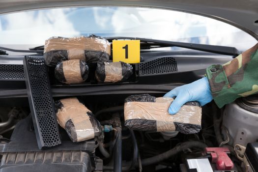 Policeman holding drug package found in engine compartment of a car