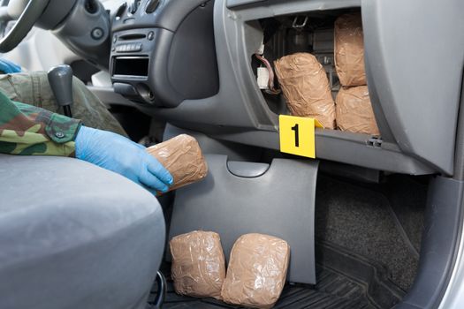 Policeman holding drug package discovered in secret compartment in a car