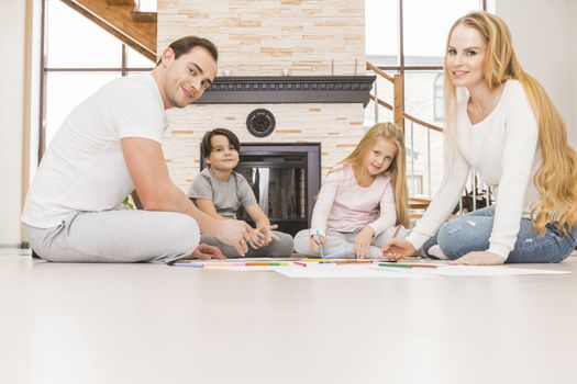 Family with two children drawing together in a living room sitting on the floor