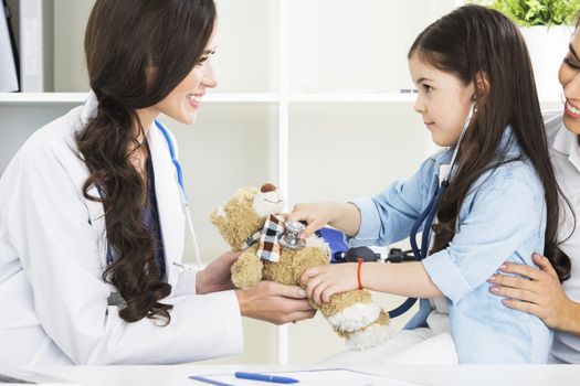 Young smiling female doctor and her little patient with teddy bear