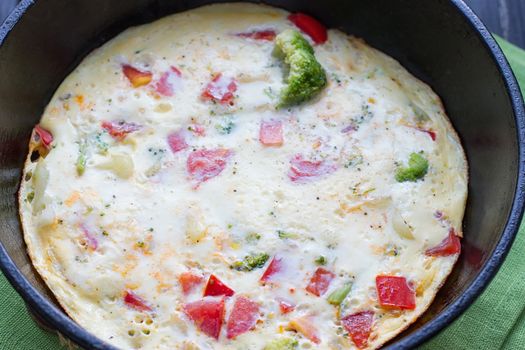 Cooking omelet in a pan, ready to serve. With tomatoes, red onion, goat's cheese and parsley