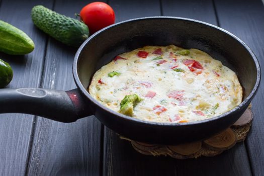 Breakfast set. Pan of fried eggs with fresh tomato, cucumber, sage on dark serving board over black background