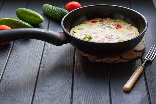 Breakfast set. Pan of fried eggs with fresh tomato, cucumber, sage on dark serving board over black background