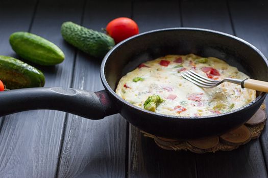 Breakfast set. Pan of fried eggs with fresh tomato, cucumber, sage on dark serving board over black background