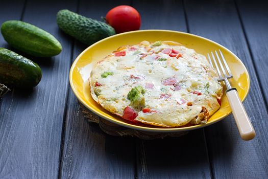 Hearty and tasty breakfast, traditional in the hotel, omelette from chicken eggs with cheese, fresh vegetables - cucumber and tomato on the black wooden background