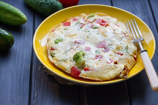 Hearty and tasty breakfast, traditional in the hotel, omelette from chicken eggs with cheese, fresh vegetables - cucumber and tomato on the black wooden background