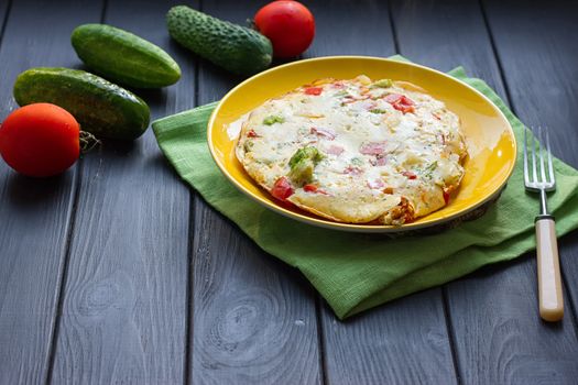 Hearty and tasty breakfast, traditional in the hotel, omelette from chicken eggs with cheese, fresh vegetables - cucumber and tomato on the black wooden background