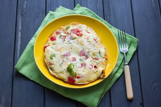 Hearty and tasty breakfast, traditional in the hotel, omelette from chicken eggs with cheese, fresh vegetables - cucumber and tomato on the black wooden background